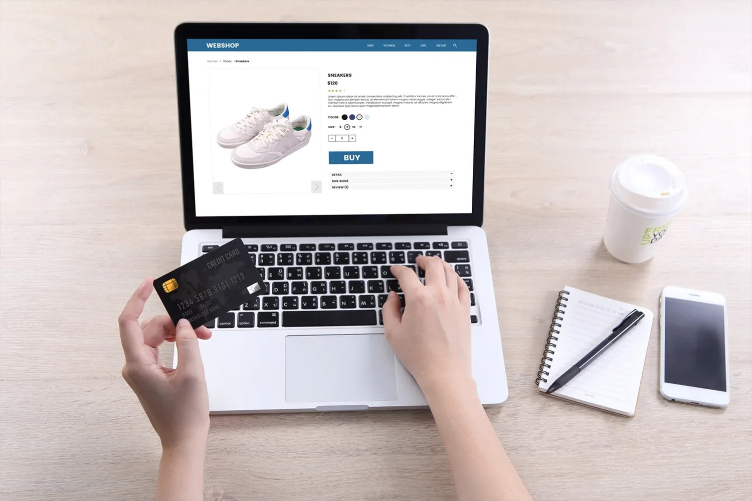 Hände, die bei einer Schuhbestellung im Onlineshop Kartendaten eingeben; auf dem Tisch Smartphone, Notizbuch und Kaffee